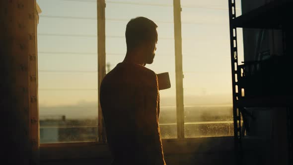 Silhouette of boy drinks tea at the window