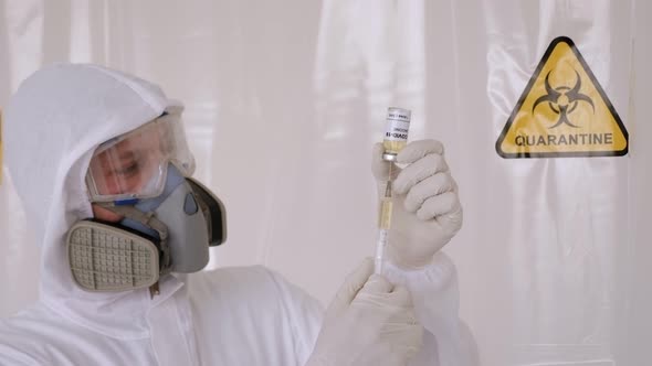 A Doctor in a Medical Suit Holding a Coronavirus Vaccine and a Syringe