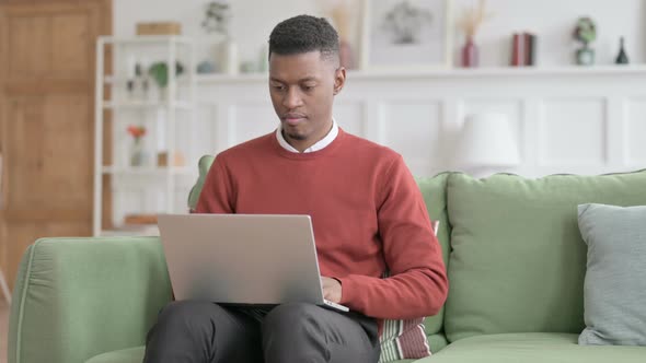 African Man Looking at Camera while using Laptop on Sofa