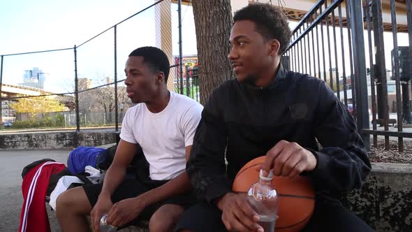 Two young basketball players drinking water while taking a break from playing.