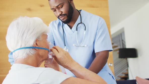 Video of african american male doctor keeping oxygen to caucasian senior woman