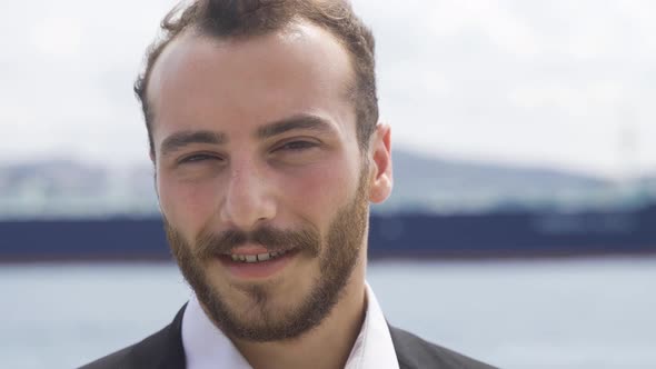 Smiling businessman looking at camera by the sea.