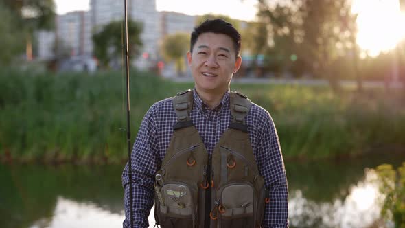 Portrait of the Smiled Fisherman Wearing Special Clothes for Fishing Holding the Fishing Rod