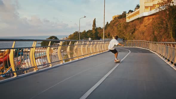 Back View of Millennial Guy Skateboarding on City Bridge Slow Motion