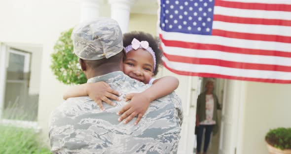 African american male soldier embracing his smiling daughter over american flag