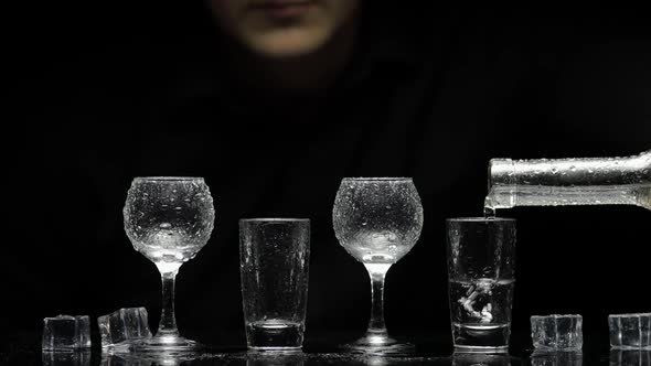 Barman Pour Frozen Vodka From Bottle Into Glasses with Ice. Black Background