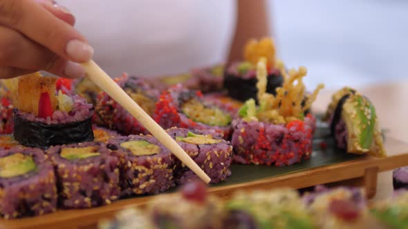 Hand Picking One Colorful Sushi Roll with Chopsticks. Artisan Asian Street Food Concept