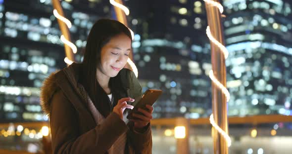 Woman sending sms on smart phone in city at night with city building background