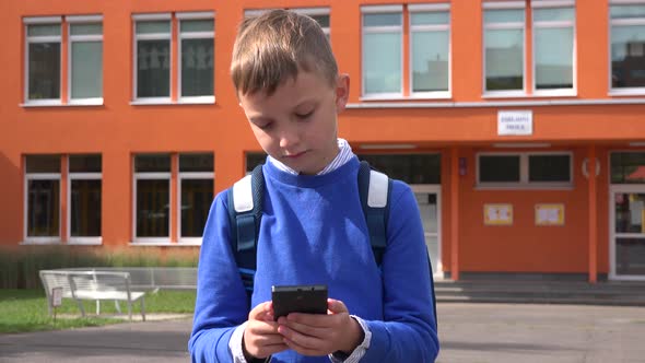 A Young Boy Works on a Smartphone in Front of an Elementary School