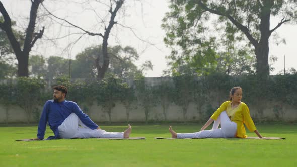 Half Spinal Twist Yoga pose or Ardha Matsyendrasana is being done by an Indian couple