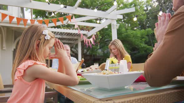 Three generation family praying before having lunch outdoors