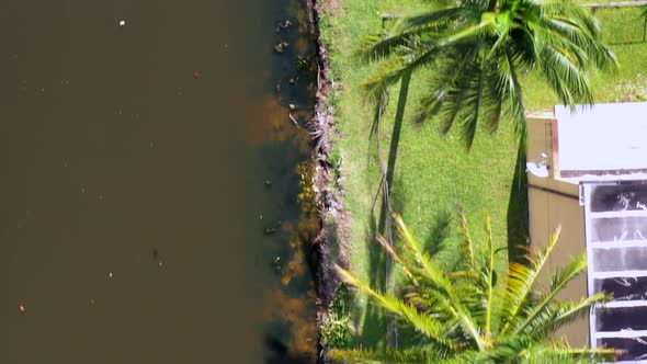 A top down view over a dirty water runoff behind residential homes with green grass and palm trees.