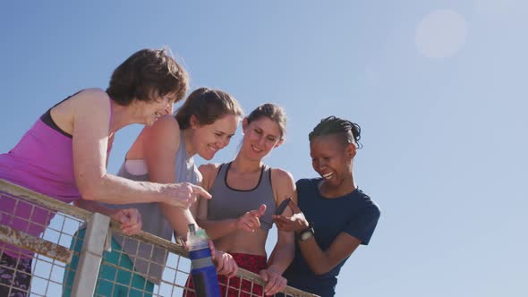 Multi-ethnic group of women laughing and using a phone on the beach and blue sky background