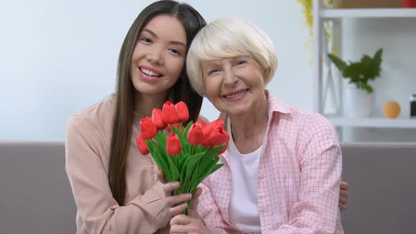 Hugging Grandmother and Granddaughter With Bouquet of Tulips Looking at Camera