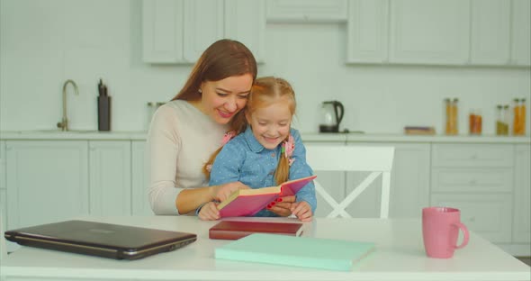 Carefree Mum and Daughter Reading Book in Kitchen