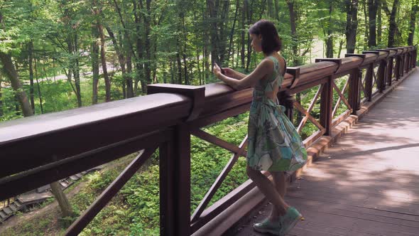 A Girl Stands at the Rail on the Bridgework in the Park and Writing Mail