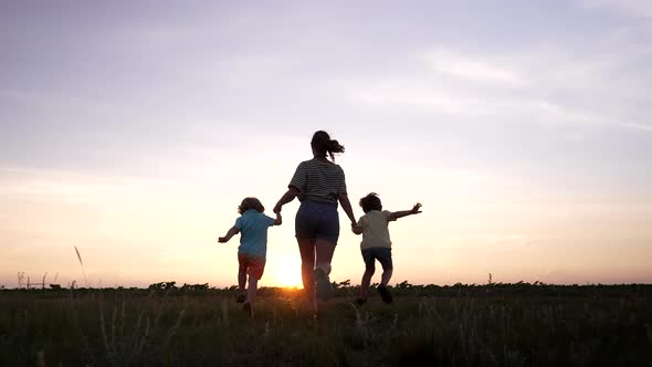 Silhouette of Young Family Mom and Two Brothers Twins Boys Runs to Sun on Open Air Field or Park