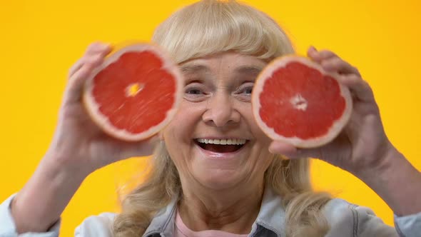 Cheerful Aged Woman Holding Grapefruit Slices Front of Eyes, Fruits Nutrition