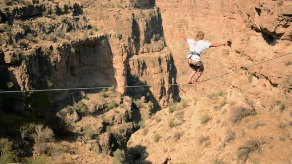 Aerial view of a woman balancing while tightrope walking and slacklining across a canyon