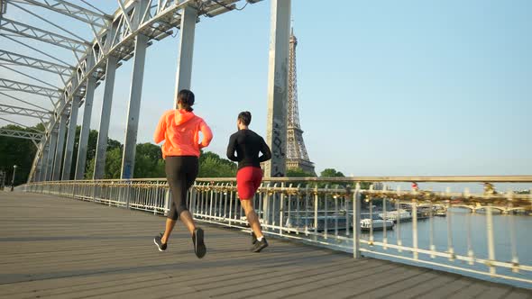 A man woman couple running across a bridge with the Eiffel Tower