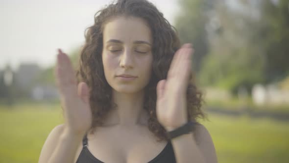 Close-up Portrait of Confident Brunette Curly-haired Woman Putting Hands Together, Closing Eyes