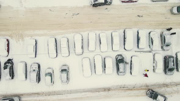 Cars Stand in a Row Covered with Snow After a Blizzard and Drive Along the Road