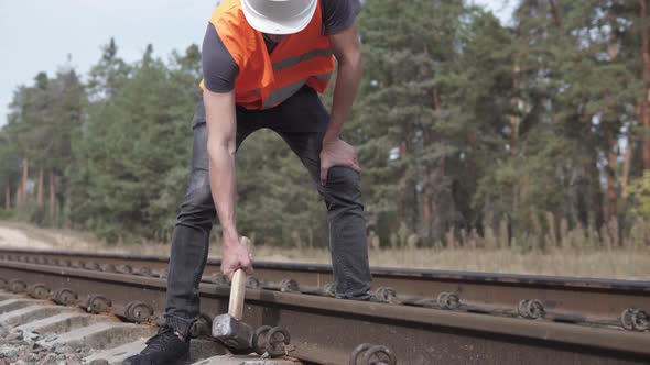 A Railway Man in a Helmet Repairs a Railway, Hammering the Spire with a Sledgehammer	