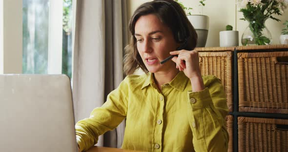 Midsection of caucasian woman talking on phone headset using laptop working from home
