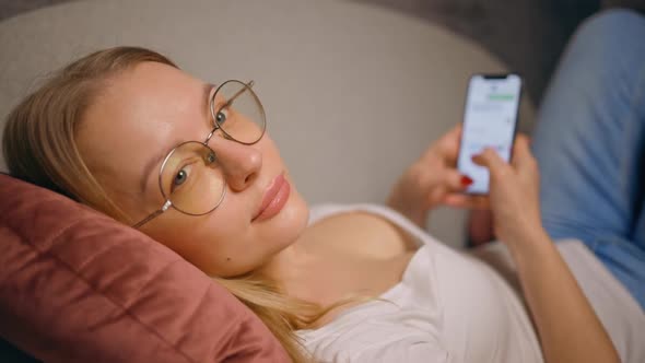Woman in Glasses Looks at you Turns Away to Start Texting Using Mobile Phone Lying on Sofa