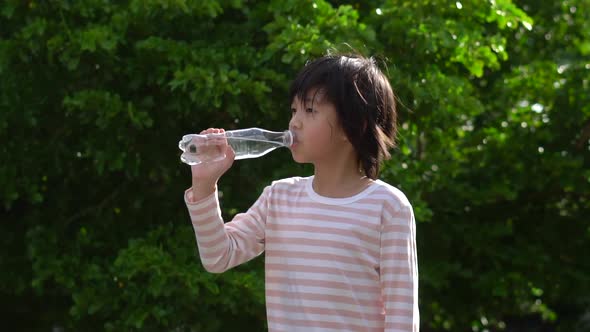 Cute Asian Child Drinking Water From A Bottle Outdoor