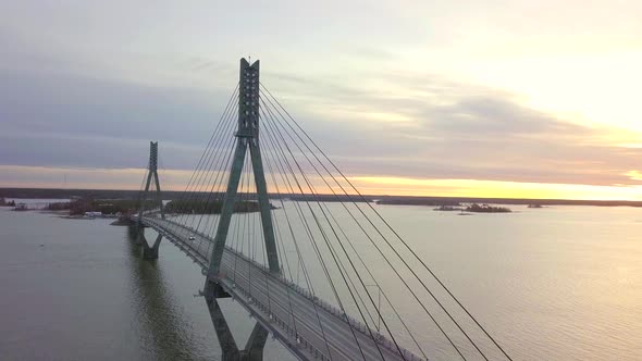 Aerial of white car driving over long bridge over body of water at stunning golden sunrise