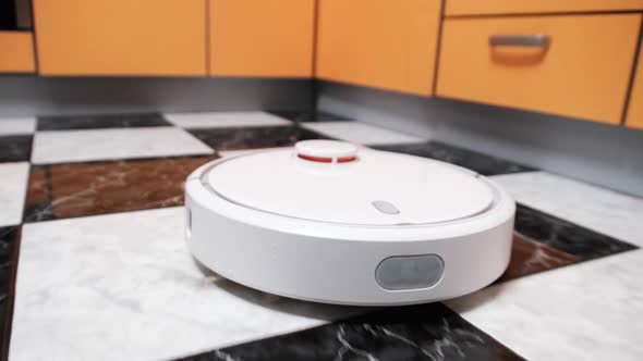 The Robot Vacuum Cleaner Cleans in the Modern House on the Tiles Floor at Kitchen