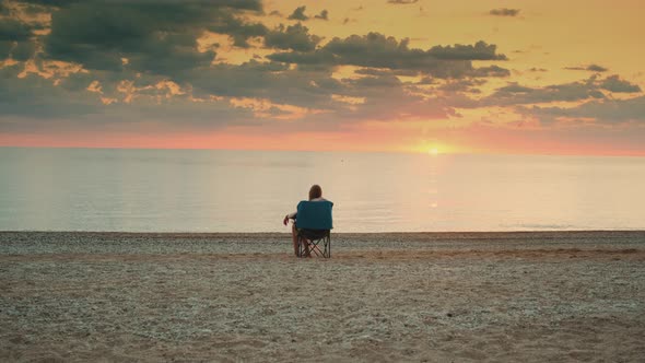 View of Lady Admiring Sunset on the Sea Sitting in Folding Tourist Chair