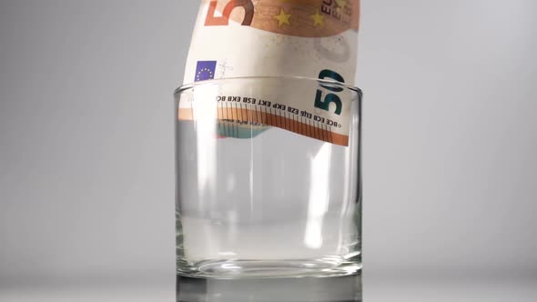 Hand puts a wad of money with a banknote of 50 euros in a glass 