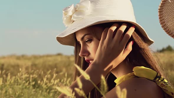 Teenager in a Hat Sits in the Field and Adjusts His Hair. Slow Motion