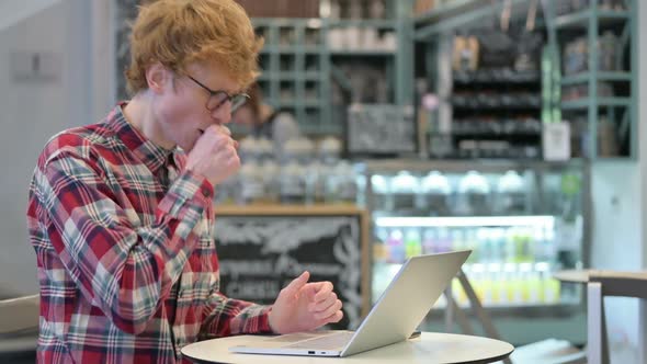 Young Redhead Man with Laptop in Cafe Coughing