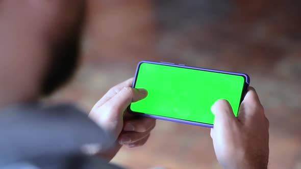Green screen phone mock up in the hands of a man playing games on a smartphone