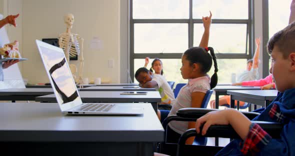 Schoolkids raising hand while sitting at desk in elementary school 4k