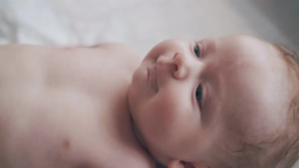 Cute Infant Boy with Bright Blue Eyes Lies on Changing Table