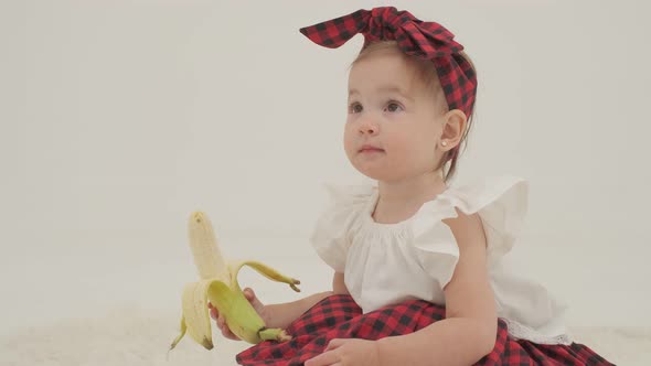 Little girl in plaid headband and skirt is holding big peeled banana