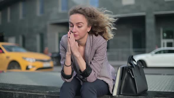 Young pensive woman is thinking about something while sitting on the street