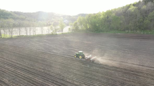 Farmer tilling field on a bright sunny day. Dry dust making a cloud behind. Mountains rising up. alt