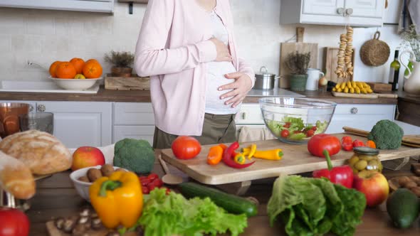Pregnant Woman Touching Her Belly While Cooking Healthy Salad On Kitchen.