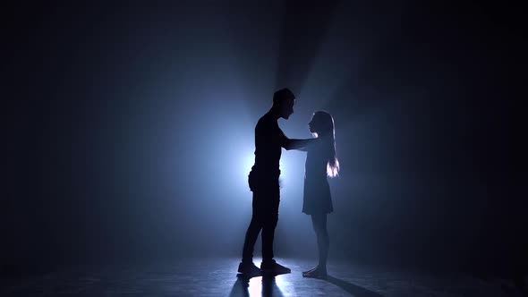 Silhouette of Couple Dancers Against Spotlight with Haze at Dark Studio.