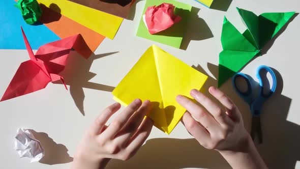 Children's Hands Do Origami From Colored Paper on White