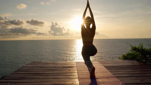 Silhouette of woman practices yoga and doing stretching at sunrise