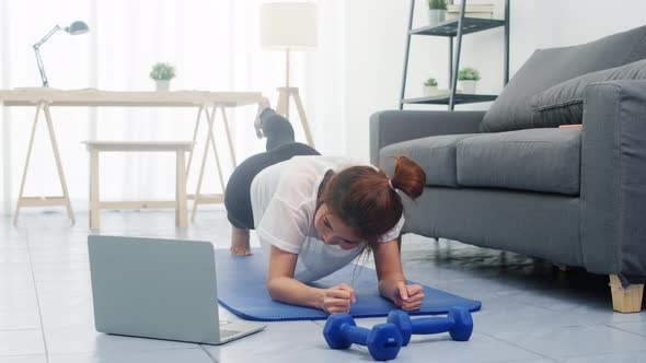 Young lady exercises doing working out and using laptop to watching yoga video tutorial at home.
