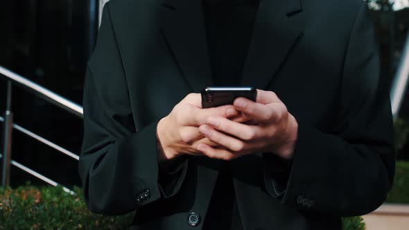 Young Caucasian Man Holding Smartphone Device Texting Sms Message Outside Business Office, Using