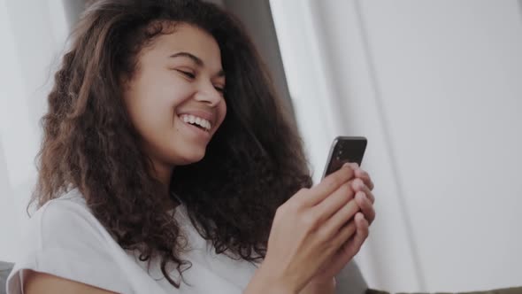 Happy Millennial African American Woman Holding Smartphone Using Ecommerce Apps Playing Mobile Games