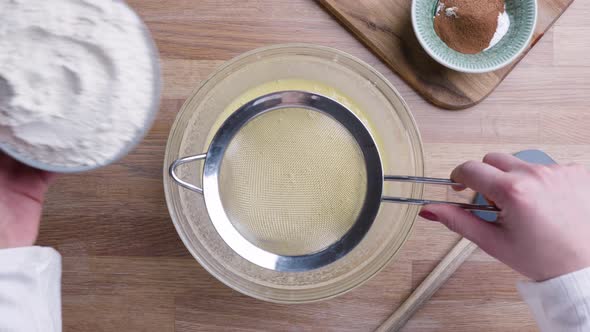 Female Baker Straining Flour To The Beaten Eggs For Carrot Cake Preparation - high angle shot